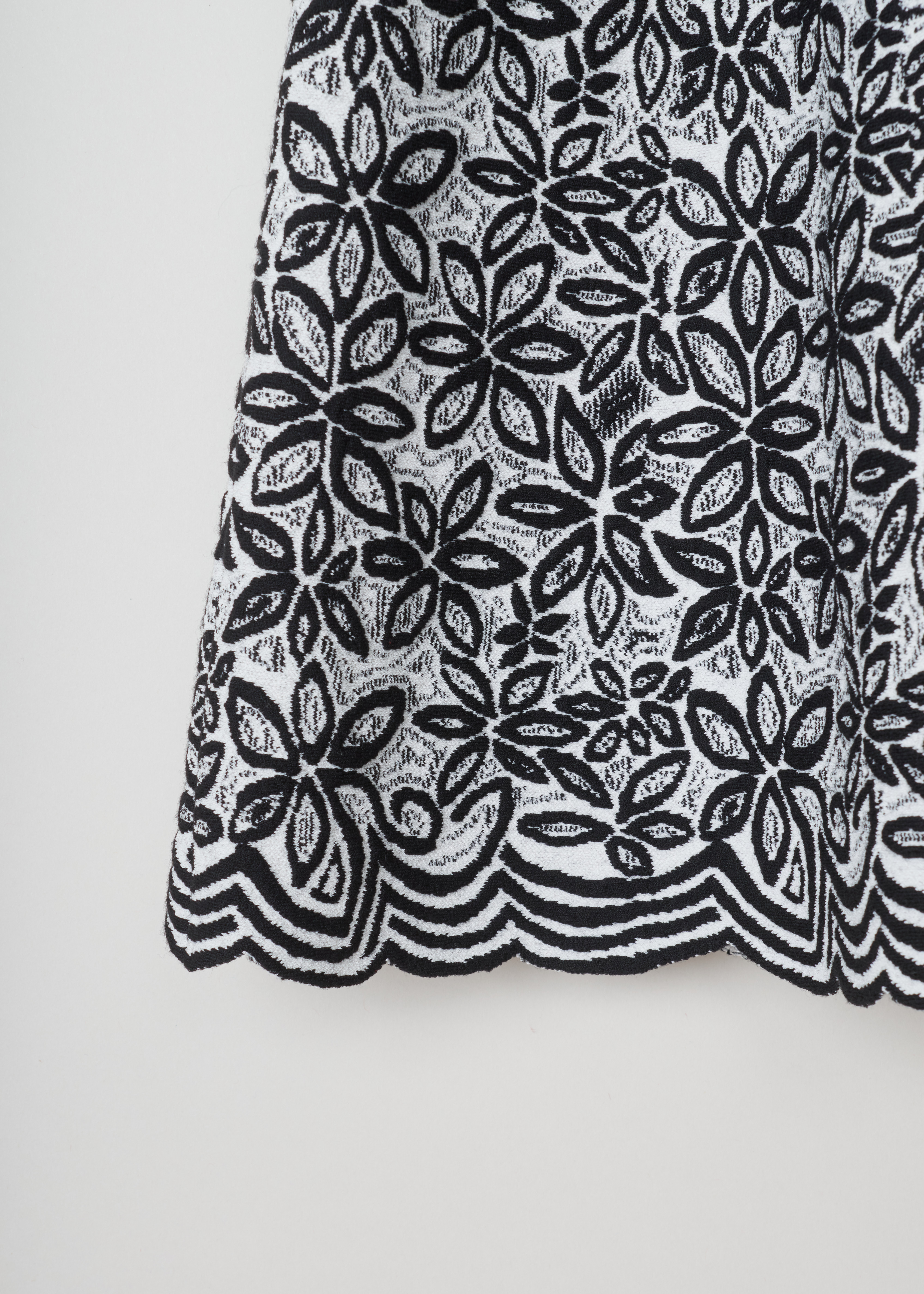 ALAÏA, Wool-blend tunic with a flower pattern, 7W9UE52RM353_TUNIQUE_ADENIUM_C009_Blanc/Noir, Grey, Print, Detail 1, Jacquard knitted tunic with a black-and-white flower motif. The dress has short sleeves, a wide round neckline, an A-line silhouette and scalloped hems.


