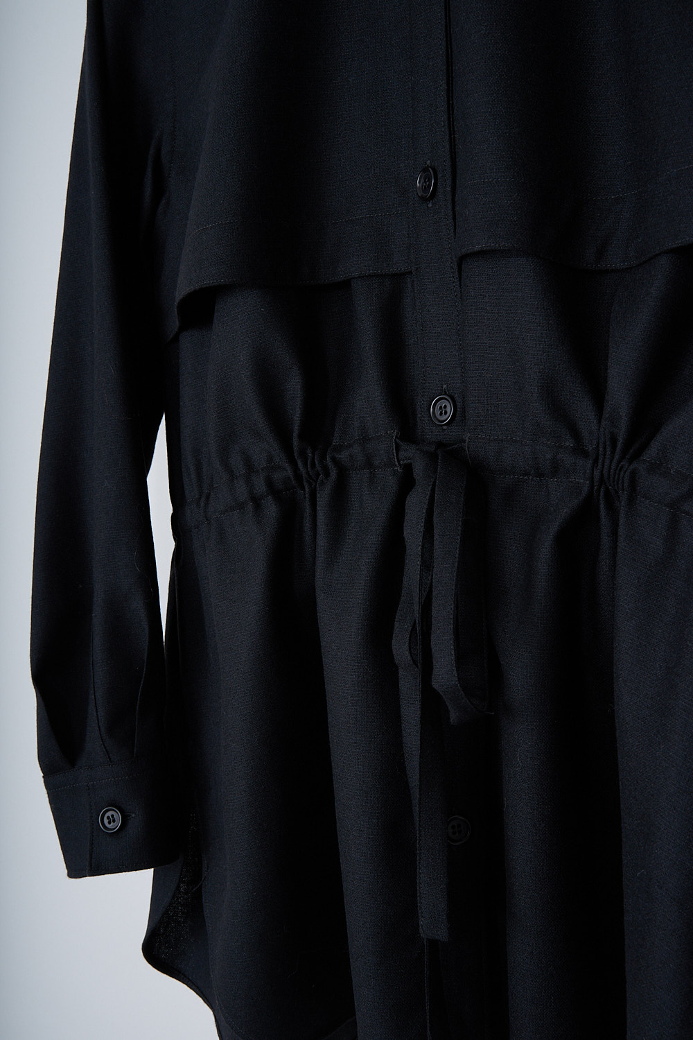 ASPESI, BLACK BLOUSE WITH DRAWSTRING DETAIL, 5457_L629_01241, Black, Detail, This black blouse has a classic collar and a button placket in the front. The long sleeves have buttoned cuffs. The blouse has a storm shield across the chest that extends to the back. A drawstring can be used to cinch in the waist. The blouse has a curved hemline.
