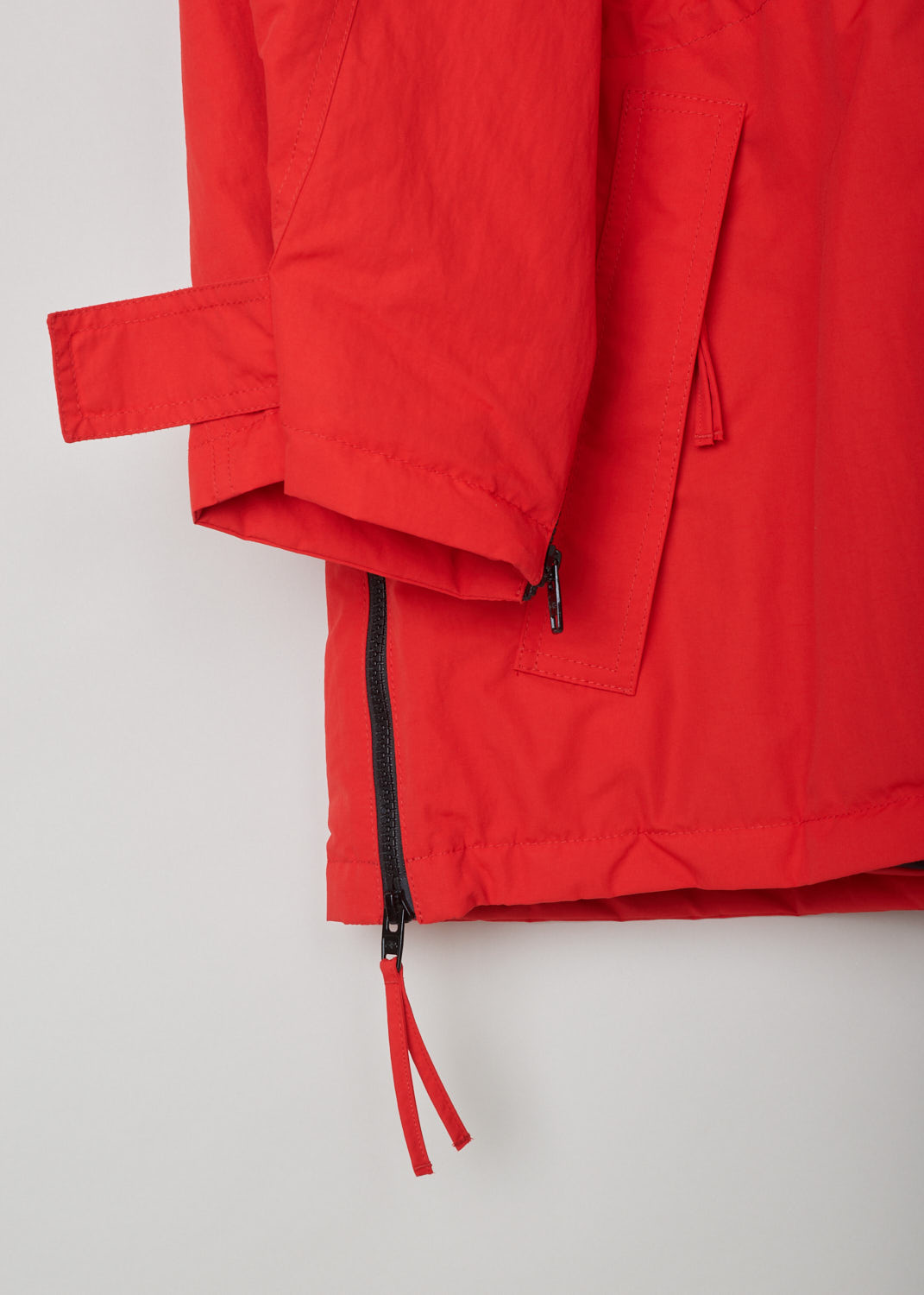 Balenciaga, Red parka model, 646774_TJ014_6400, red, detail2. Red oversized parka has lots of features beginning with the hood which is lined and detachable with press buttons. Going down this model has 4 pockets 2 on chest height 2 below that, with al the pockets being forward slanted. There is a cord tunnel on the inside with which the width of the waist can be adjusted. The fun part of this parka is the zipper which starts from the sides going up to the armpit and ending on the sleeves. Comes with zip fastening 