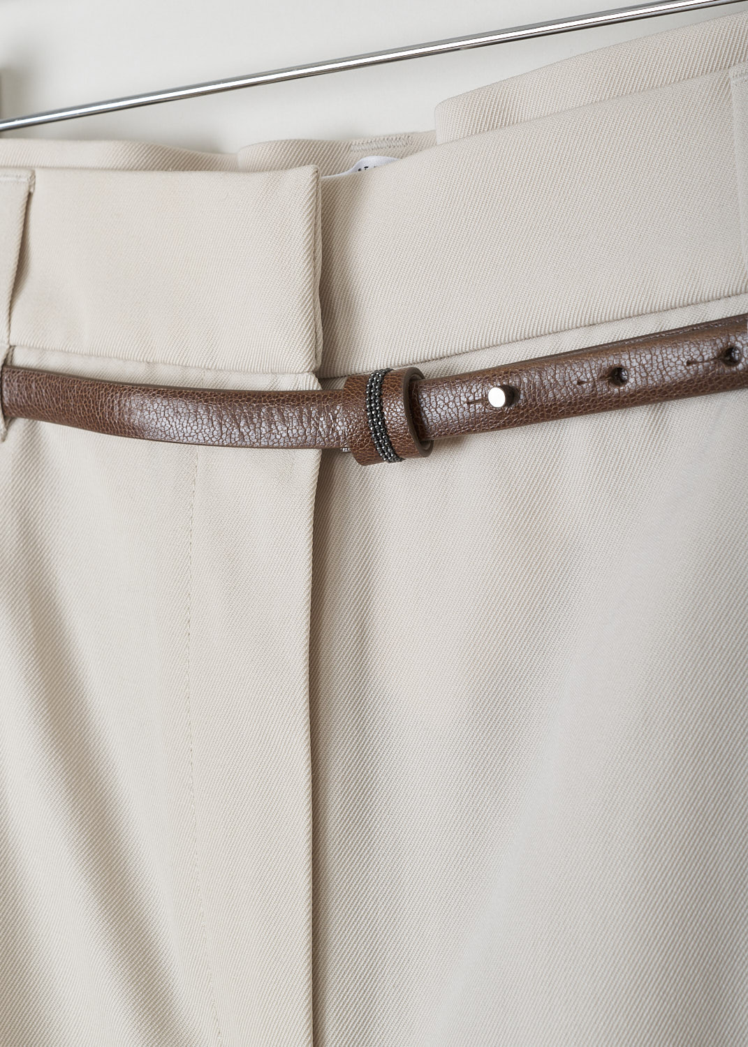 BRUNELLO CUCINELLI, BEIGE PANTS WITH TAPERED LEGS, MA033P7379_C8501, Beige, Detail 1, These beige pleated pants have a half elasticated waistband. The waistband has both broad and a narrow belt loops and comes with a brown leather belt through the narrow belt loops. A concealed snap button and zipper function as the closure option. These pants have a pleated front with tapered pant legs. Slanted pockets can be found in the front and welt pockets in the back.  
