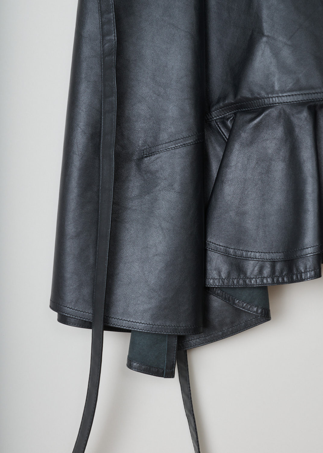 CÃ©line, Asymmetrical black leather wrap skirt, 045A_22081_ONO_C01, black, detail, Wrap skirt crafted in calf leather, the softest kind of leather. This model features a backing button on the inside. Beside that, it has two leather ribbons that can be used as fastening option, or can be tied in various decorative knots. Furthermore, this model has concealed pockets on the side seam.