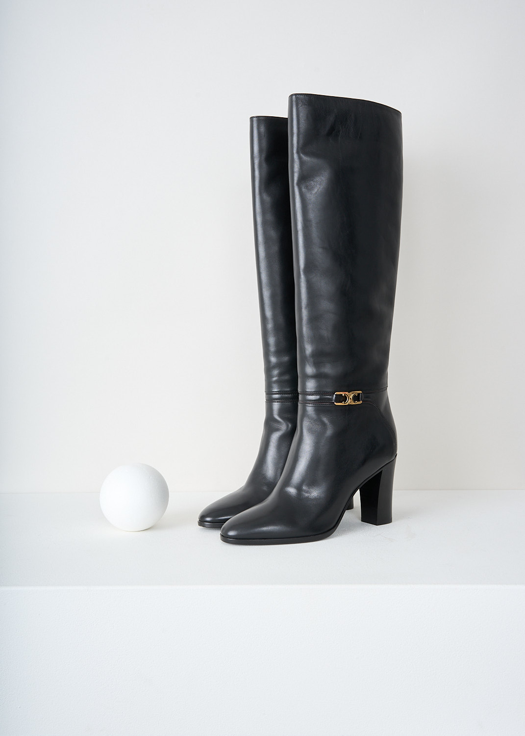 Black leather knee-high boots with almond toe and gold-tone Triomphe buckle on ankle strap by Celine, available at designer boutique Kiki's Stocksale in Maastricht.