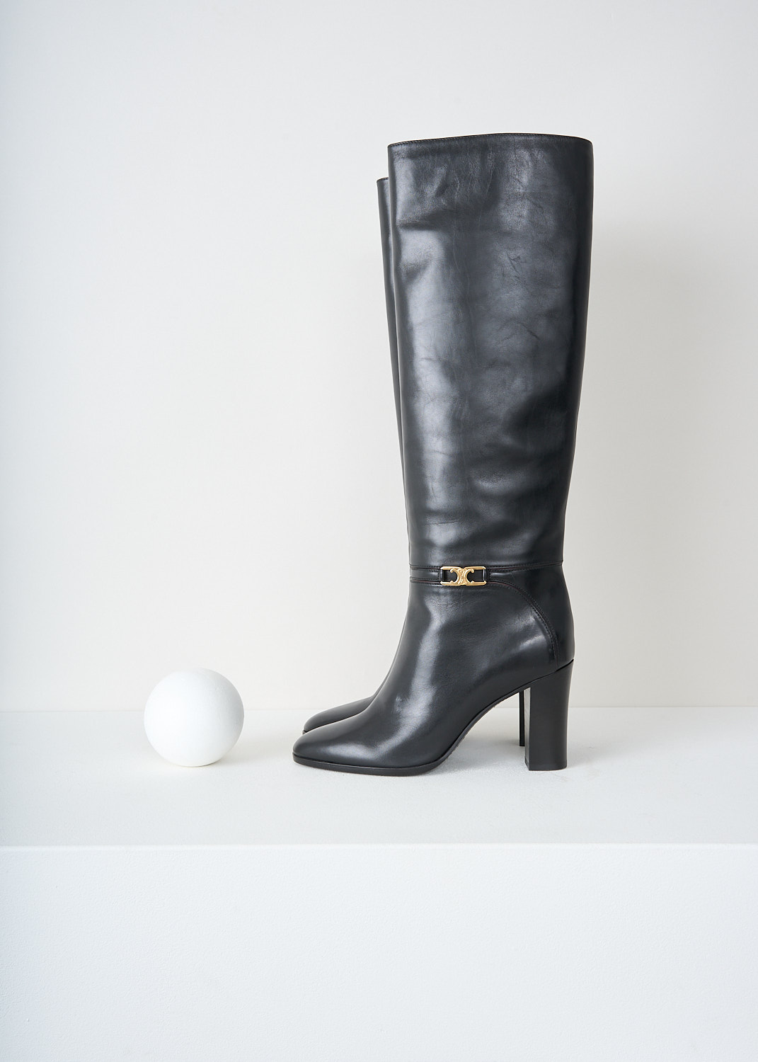 Side view of the black leather knee-high boots showing stacked block heel and ankle buckle by Celine, available at designer boutique Kiki's Stocksale in Maastricht.

