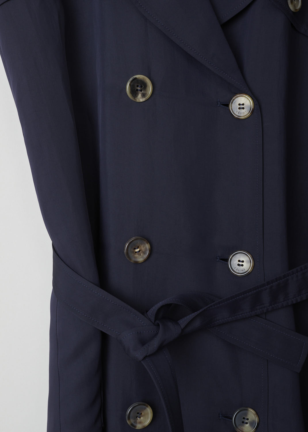 CÉLINE, MIDNIGHT BLUE RAINCOAT, 6464_28U36_0MI_C01, Blue, Detail, Elegant midnight blue trench coat. The coat has a notched lapel and classic details such as epaulets and storm flaps. Two rows of buttons form the closing option. The coat comes with a matching belt to cinch in the waist. The long sleeves have sleeve straps on the cuffs. A slanted pocket can be found on either side. In the back, the coat has a centre slit.