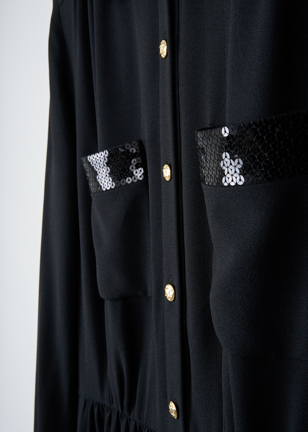 Celine, Black dress with sequins detailing, 2R25K_865C_38NO, Black, Detail, This black mini dress features a sequin-clad Claudine collar and a partial front button closure with gold-tone buttons. The long sleeves are finished with sequin-clad cuffs. On the bodice, there are two patch pockets accented with broad sequin trim. The dress has a flared skirt.
