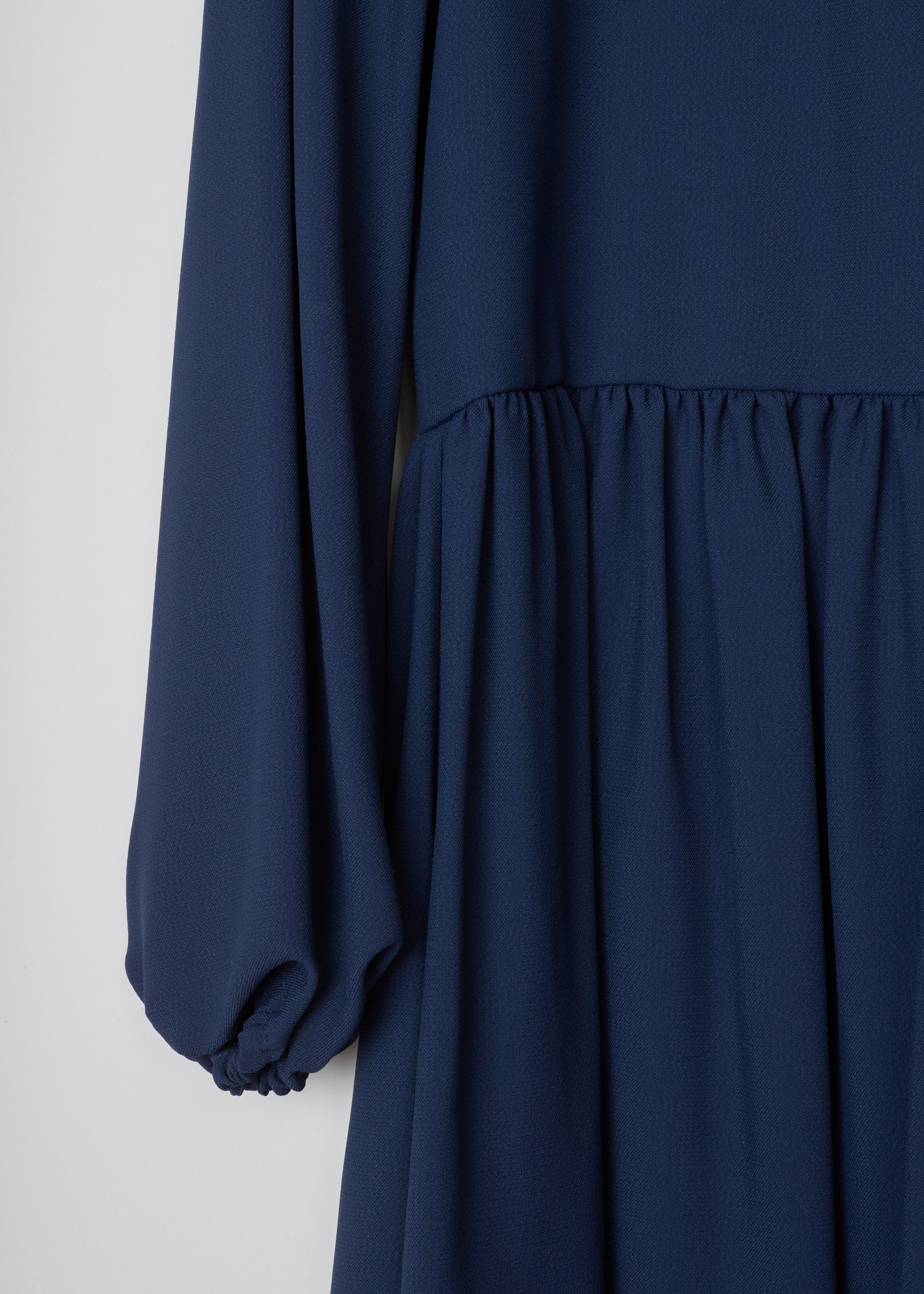 Chloé Gathered deep blue dress 17SRO65_17S37_7B5 deep blue detail. Deep blue dress with a V-neck. This model has loose sleeves and gathered cuffs. The straight cut has small pleats around the waist and a midi length. As closure this dress has an invisible zipper on the side.