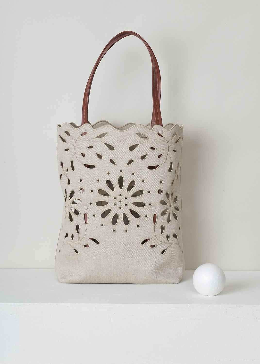 CHLOÃ‰ LARGE KAMILLA NORTH - SOUTH TOTE BAG IN SEPIA BROWN
,CHC22SS492G2327S_KAMILLA_LARGE_NORTH_SO, Beige, Front, This large Kamilla North - South tote bag in sepia brown has two tan leather top handles. The linen has a scalloped top edge and floral broderie anglaise detailing throughout. On the inside, the bag has a removable tan leather pouch with a zipper.  