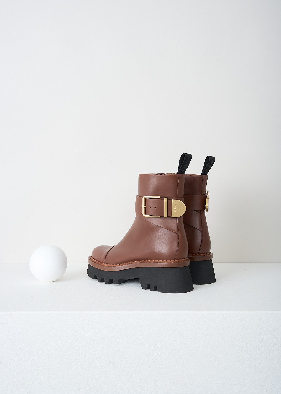 Chloé, Brunet Brown Owena ankle boots, CHC23A893EX25L_BRUNET_BROWN_F, Brown, Back, These Brunet Brown smooth leather Owena ankle boots have a gold-tone buckle that wraps around the ankle. The pull-tabs have the brand's logo on them. The boots have a zip on the inside of the leg that function as the closure option. The round toe has a seam across the vamp. These boots have black rubber platform soles.

