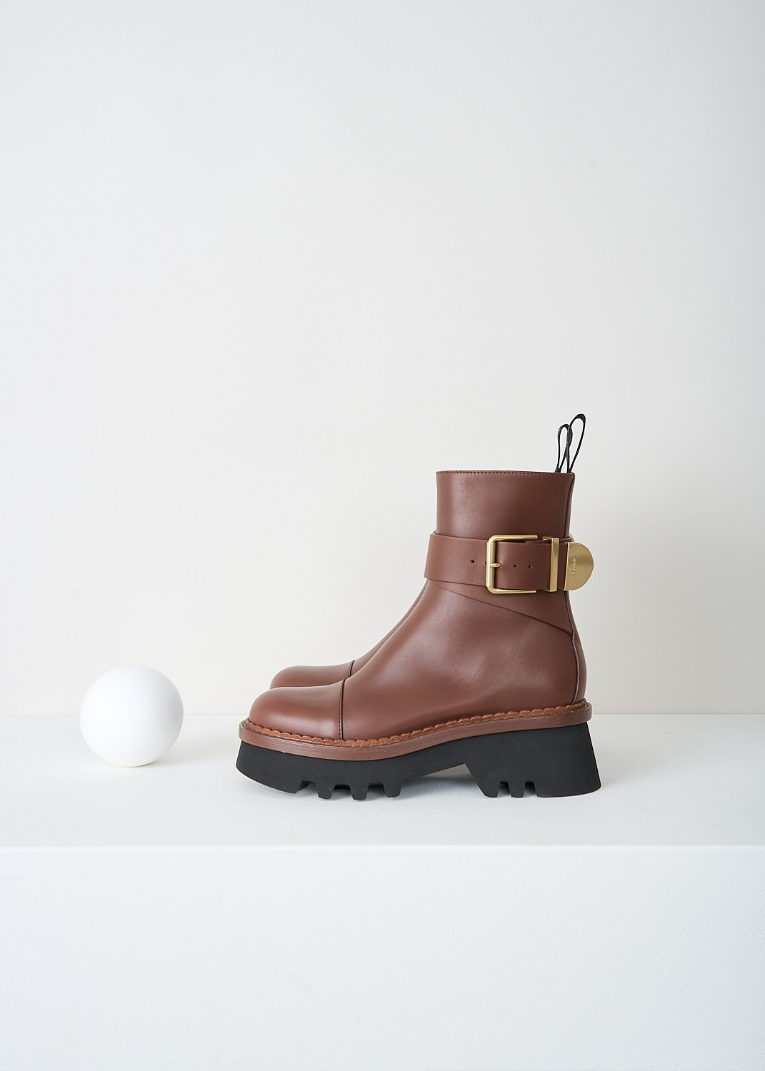 Chloé, Brunet Brown Owena ankle boots, CHC23A893EX25L_BRUNET_BROWN_F, Brown, Side, These Brunet Brown smooth leather Owena ankle boots have a gold-tone buckle that wraps around the ankle. The pull-tabs have the brand's logo on them. The boots have a zip on the inside of the leg that function as the closure option. The round toe has a seam across the vamp. These boots have black rubber platform soles.

