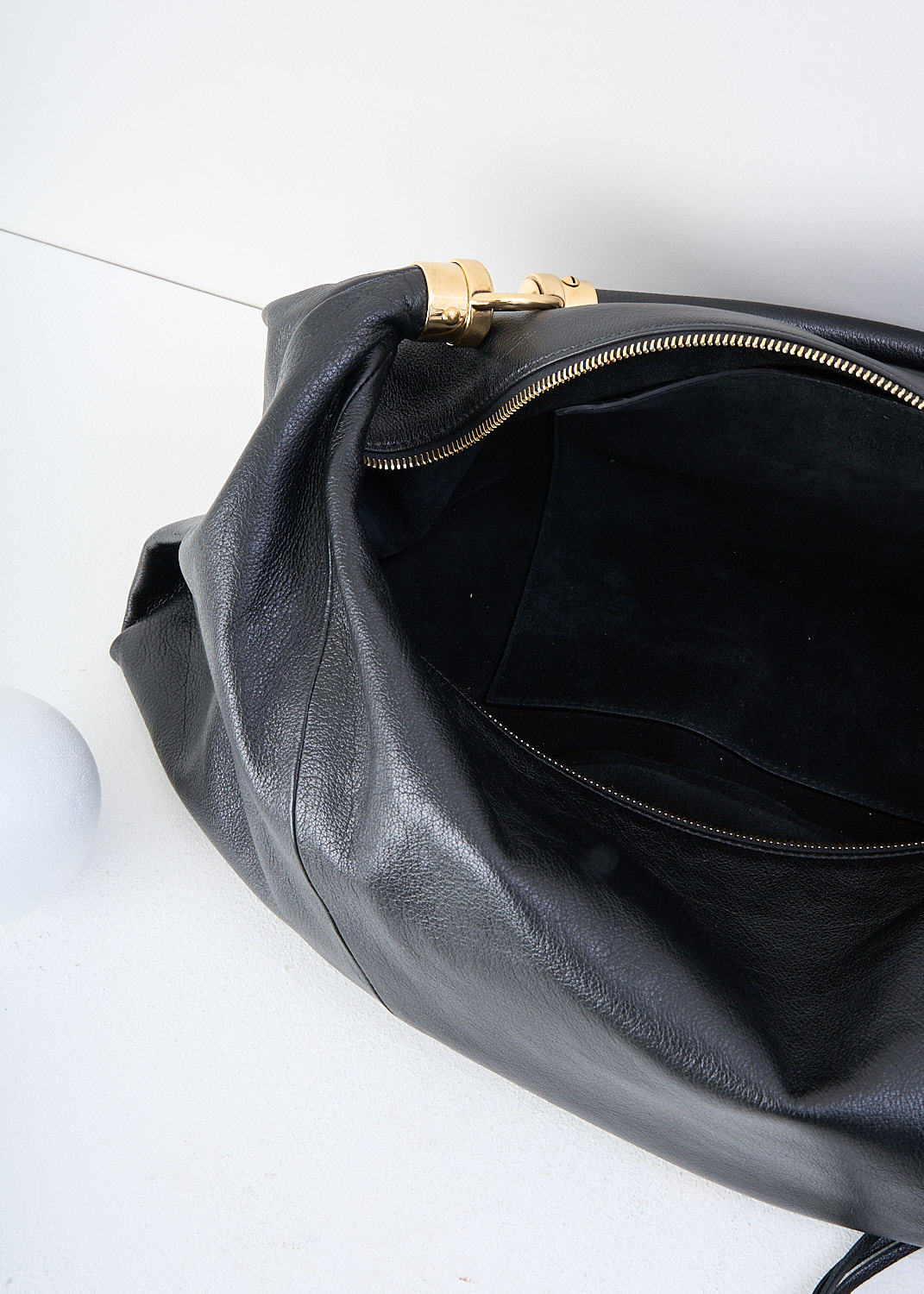 Chloé, Black foulard shoulder bag, CHC25SS446O37_001_BLACK, Black, Detail 1, This grained black buffalo leather foulard shoulder bag has a supple silhouette. The bag has a single shoulder strap with an oversized tassel and the signature gold-tone Horse Medal hardware. The top-zip opens up to the main compartment what has a slip pocket.

