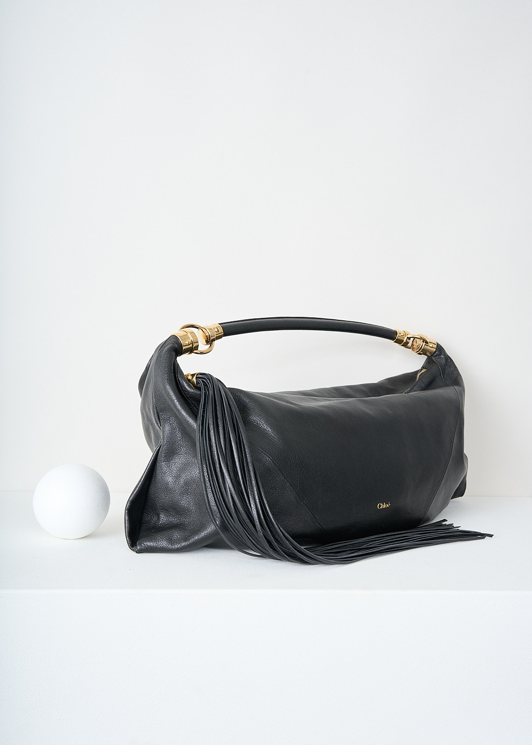 Chloé, Black foulard shoulder bag, CHC25SS446O37_001_BLACK, Black, Side, This grained black buffalo leather foulard shoulder bag has a supple silhouette. The bag has a single shoulder strap with an oversized tassel and the signature gold-tone Horse Medal hardware. The top-zip opens up to the main compartment what has a slip pocket.

