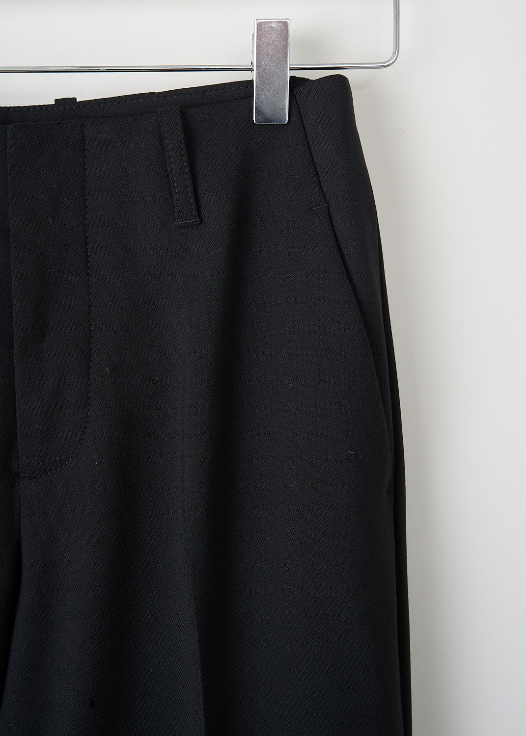 Detail of concealed clasp-and-zip closure on black slim tailored trousers.