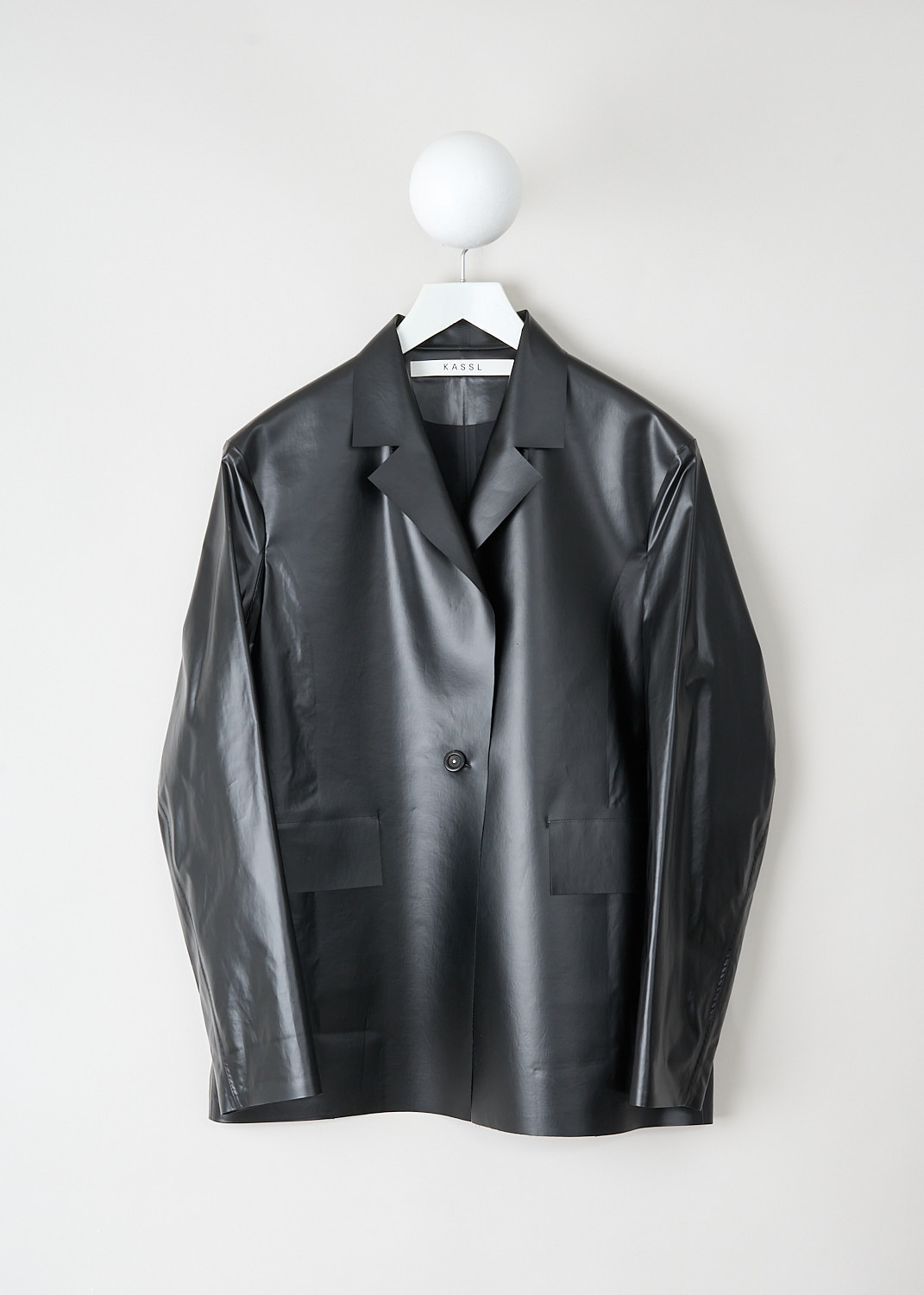 Light black oversized jacket by Kassl in oil-coated cotton with notched lapel, single button closure and flap pockets, available at Kiki’s Stocksale Maastricht designer outlet.