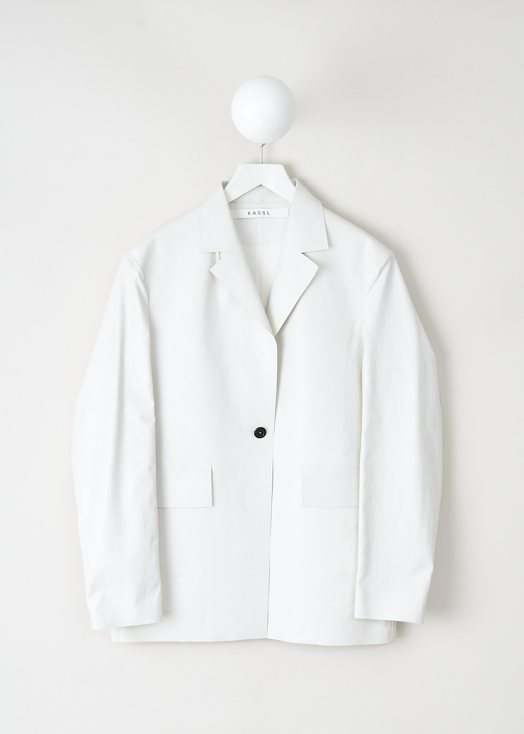 White oversized jacket by Kassl in oil-coated cotton with notched lapel, single button closure and flap pockets, available at Kiki’s Stocksale Maastricht designer outlet.