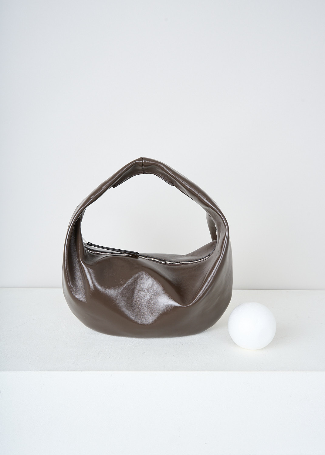 Khaite, Chestnut brown Olivia Hobo shoulder bag in medium, OLIVIA_HOBO_MEDIUM_H6015_877_934_CHESTNUT, Brown, Front, This medium Olivia Hobo shoulder bag in patent leather chestnut brown has a single top handle. The zipped top closure opens up to the main compartment with, to one side, a slip pocket. The bag has a curved silhouette. 
