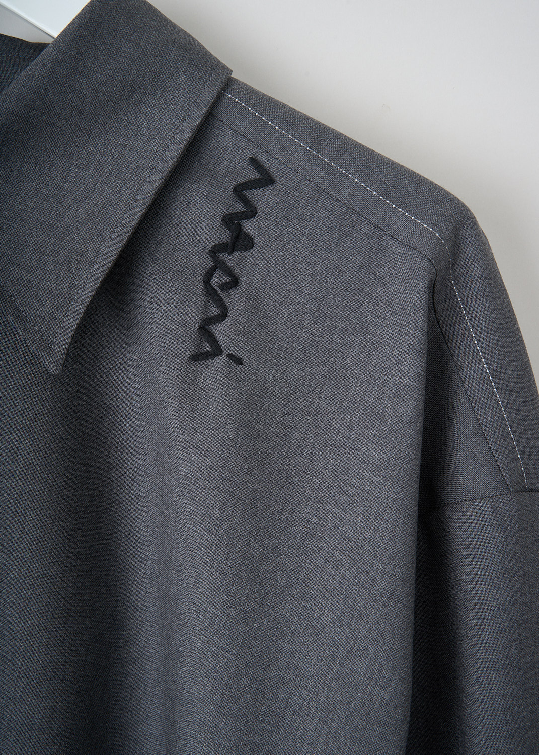 Close-up detail of Marni grey wool shirt showing embroidered logo, white layered sleeve detail and crystal pleat back yoke
