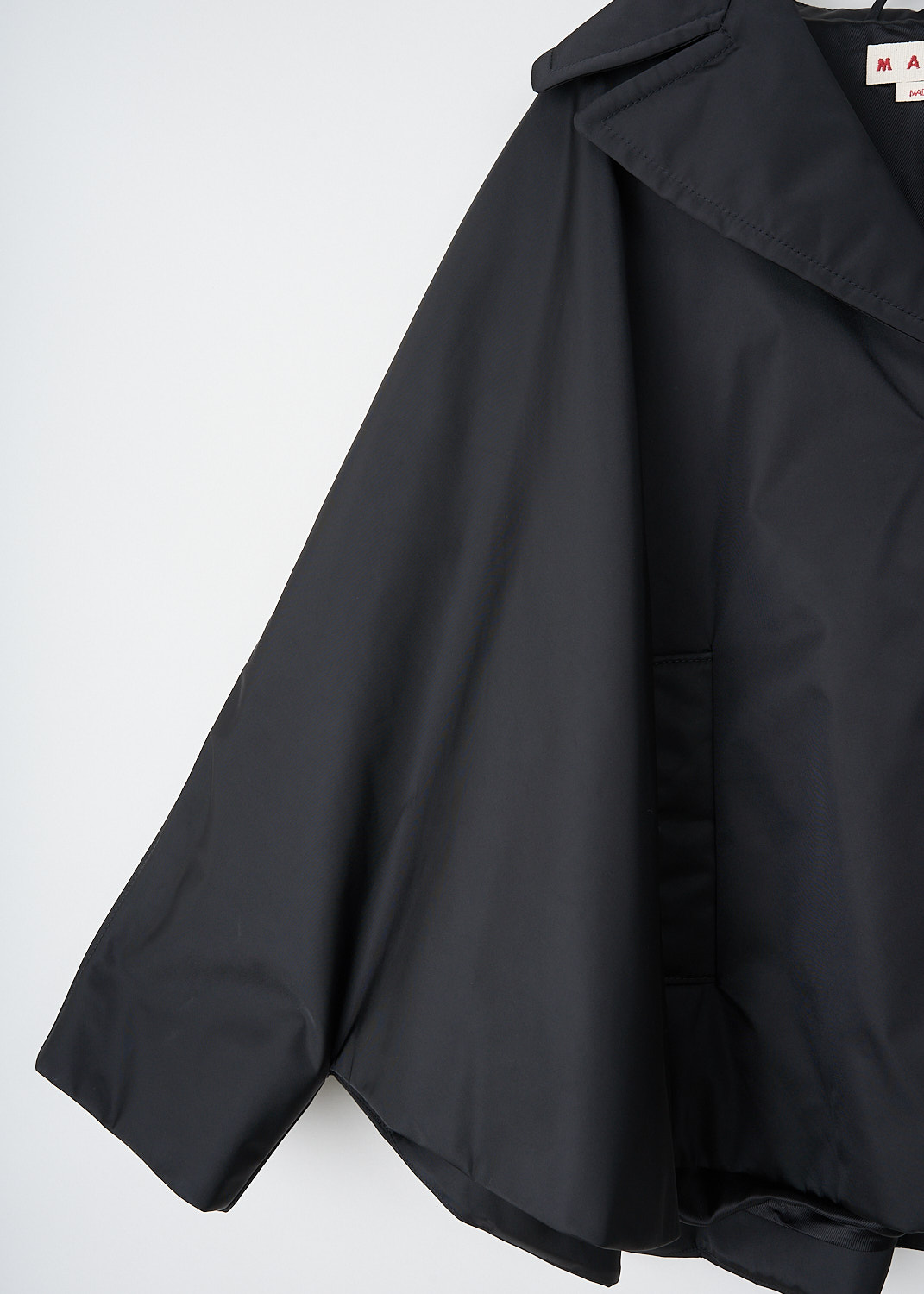 Marni, Twill cape coat in black, CPMA0251SW_UTN923_00N99, Black, Detail, This short black twill-weave cape coat has a notched lapel and a front button closure. The coat has long sleeves and a high-low hemline.  On the front, the coat has two slanted pockets. The coat has a loose fit. The coat is fully lined.
