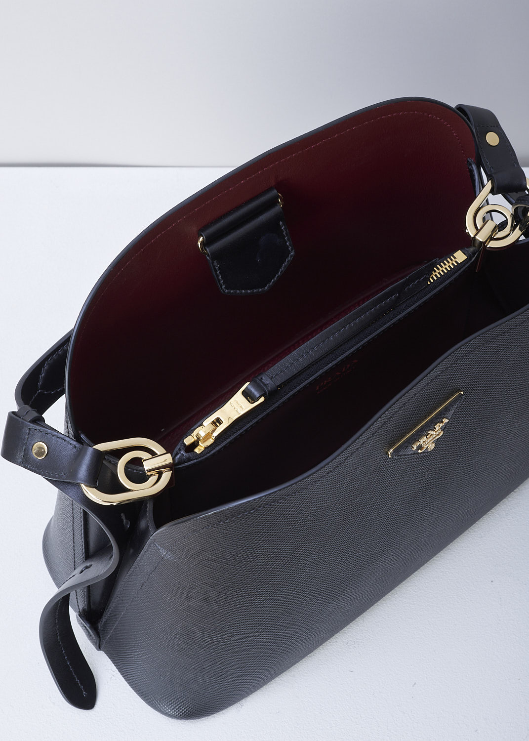 PRADA, SMALL MATINÃ‰E SHOULDER BAG IN BLACK, SAFFIANO_CUIR_C_1BA251_NERO_CERISE, Black, Detail 1, This small black MatinÃ©e shoulder bag is made with Saffiano leather. Both the leather handle and shoulder strap are adjustable and detachable. The bag has gold-tone metal hardware with the brand's triangle logo plaque on the front. The open top has a magnetic snap closure in the middle. The cherry red interior has a centre zip pocket that divides the main compartment into two spacious sides. The bag has a removable leather keychain.  


