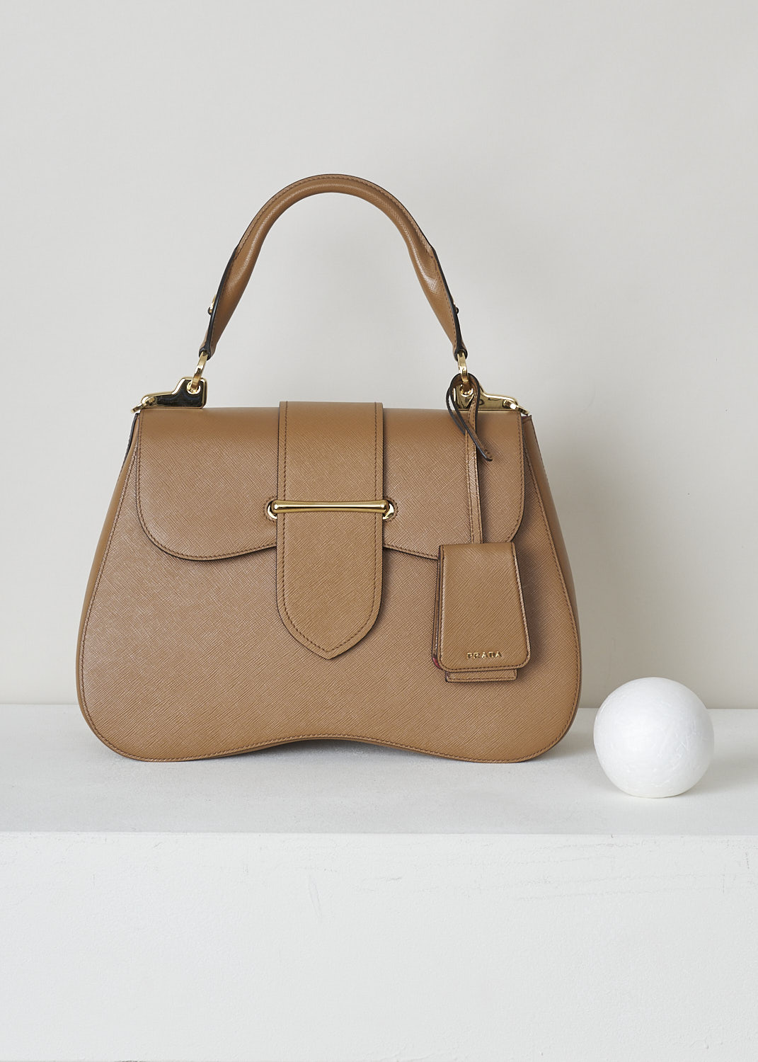 PRADA, CARAMEL BROWN SIDONIE TOP HANDLE BAG, CARTELLA_1BN002_F098L_CARAMEL, Brown, Front, This large caramel brown Sidonie Top Handle Bag is made with Saffiano leather. The bag comes with a leather handle and an adjustable and detachable shoulder strap. The bag has gold-tone metal hardware with the brand's logo on the back. The removable leather keychain has that same gold-tone logo on it. The slip-through closure opens up to reveal its red interior. The bag has a single, spacious compartment with a zipped inner pocket to one side and a patch pocket on the other side.   
