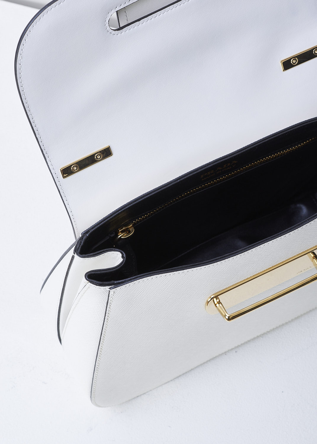 PRADA, MEDIUM SIDONIE TOP HANDLE BAG IN WHITE, CARTELLA_1BN005_F0009_BIANCO, White, Detail 1, This mid-sized white Sidonie Top Handle Bag is made with Saffiano leather. The bag comes with a leather handle and an adjustable and detachable shoulder strap. The bag has gold-tone metal hardware with the brand's logo on the back. The removable leather keychain has that same gold-tone logo on it. The slip-through closure opens up to reveal its black interior. The bag has a single, spacious compartment with a zipped inner pocket to one side and a patch pocket on the other side.  
