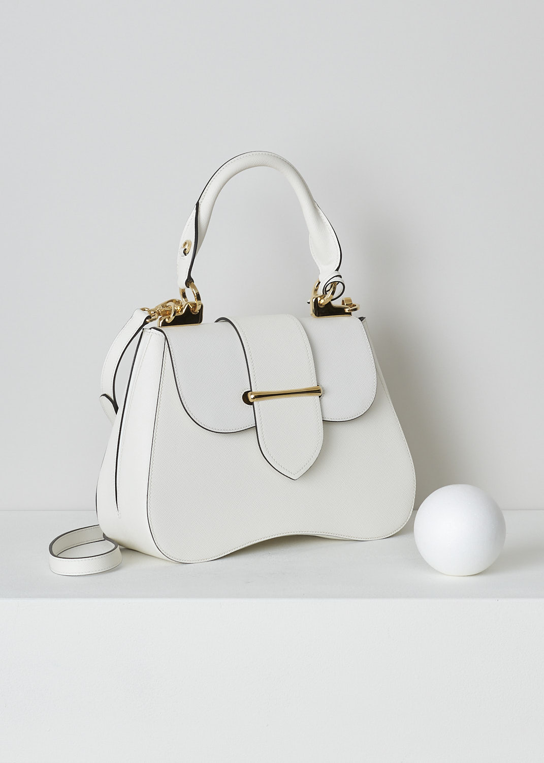 PRADA, MEDIUM SIDONIE TOP HANDLE BAG IN WHITE, CARTELLA_1BN005_F0009_BIANCO, White, Side, This mid-sized white Sidonie Top Handle Bag is made with Saffiano leather. The bag comes with a leather handle and an adjustable and detachable shoulder strap. The bag has gold-tone metal hardware with the brand's logo on the back. The removable leather keychain has that same gold-tone logo on it. The slip-through closure opens up to reveal its black interior. The bag has a single, spacious compartment with a zipped inner pocket to one side and a patch pocket on the other side.  
