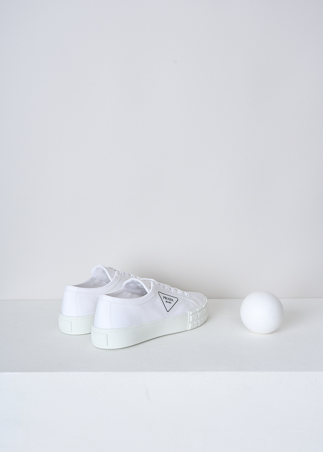 PRADA, ALL-WHITE CANVAS SNEAKERS, GUD_GABARDINE_1E939L_F0009_BIANCO, White, Back, These low top all-white canvas sneakers feature a front lace-up fastening with white laces. The brand's triangle logo can be found on the side in black. These sneakers have a round toe with a white rubber toe cap and ribbed rubber soles.
