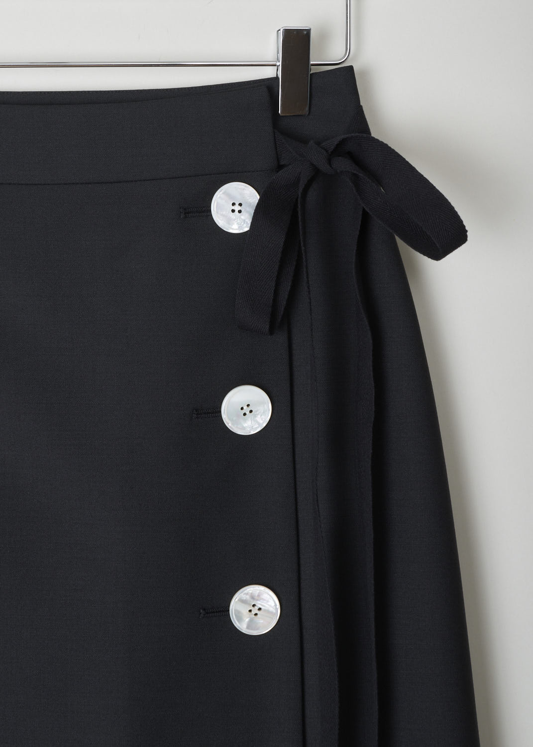 PRADA, BLACK WRAP SKIRT WITH BUTTONS AND TIE DETAIL, 
KID_MOHAIR_P122R_NERO, Black, Detail, Black wrap skirt with three contrasting mother-of-pearl buttons on the side. Above the buttons, a black ribbon tie detail can be found. Both the buttons and the tie function as the closure option, as well as a concealed button and hook on the inside. 