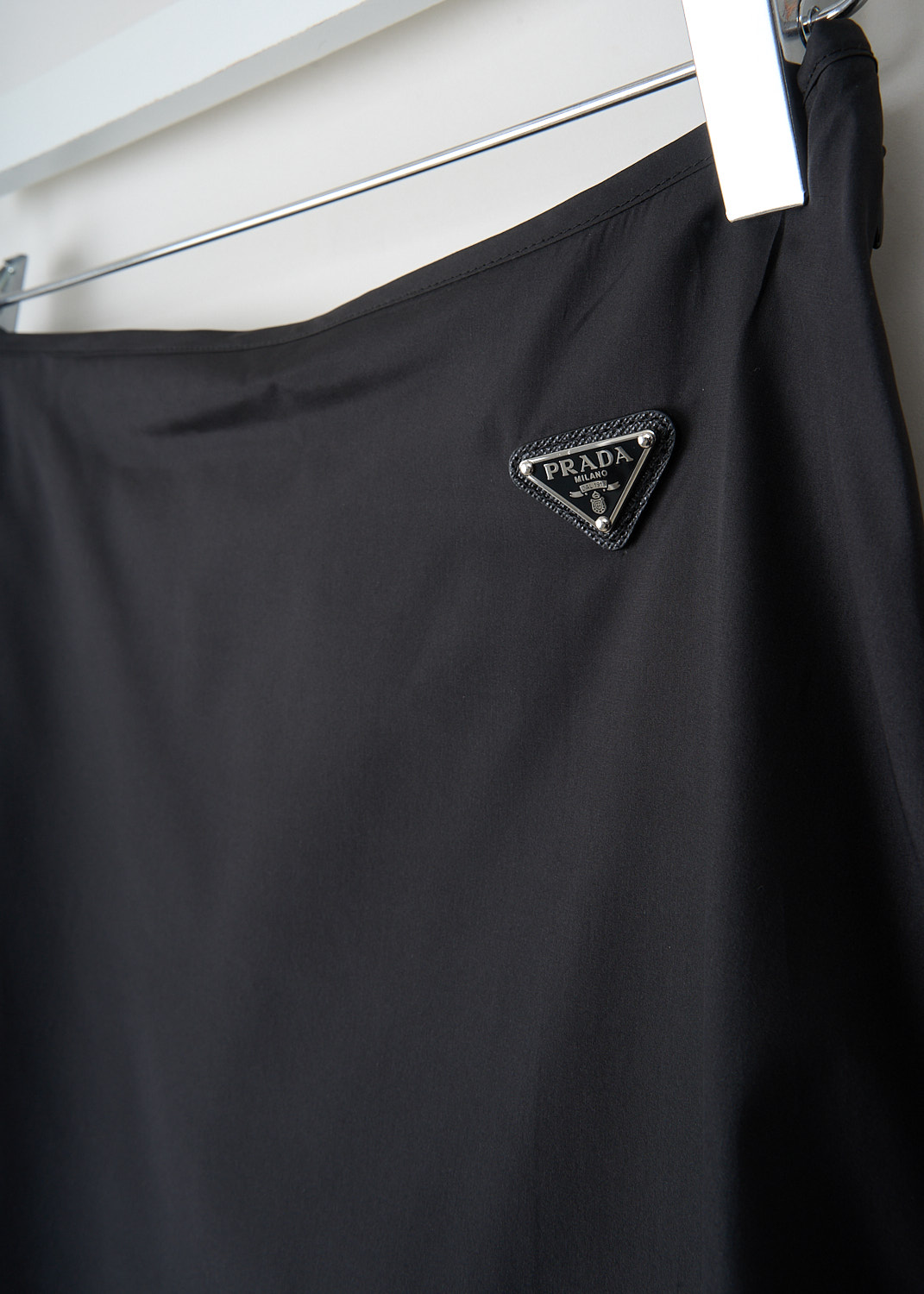 Close-up of enamelled metal triangle logo on black silk Prada slip skirt at Kiki's Stocksale designer outlet boutique in Maastricht.