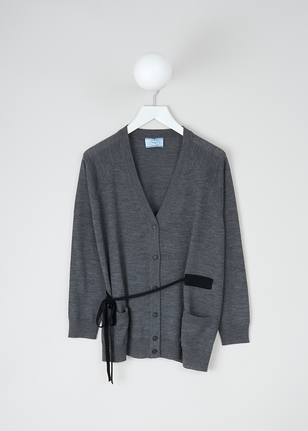 Prada, Grey V-neck cardigan with tie detail, P25E97_1NOR_F0480_ARDESIA, Grey, Front, This grey wool cardigan has a V-neckline and a front button closure. The long sleeves have ribbed cuffs. On the front, the cardigan has two patch pockets. A contrasting black tie can be used to cinch in the waist. 
