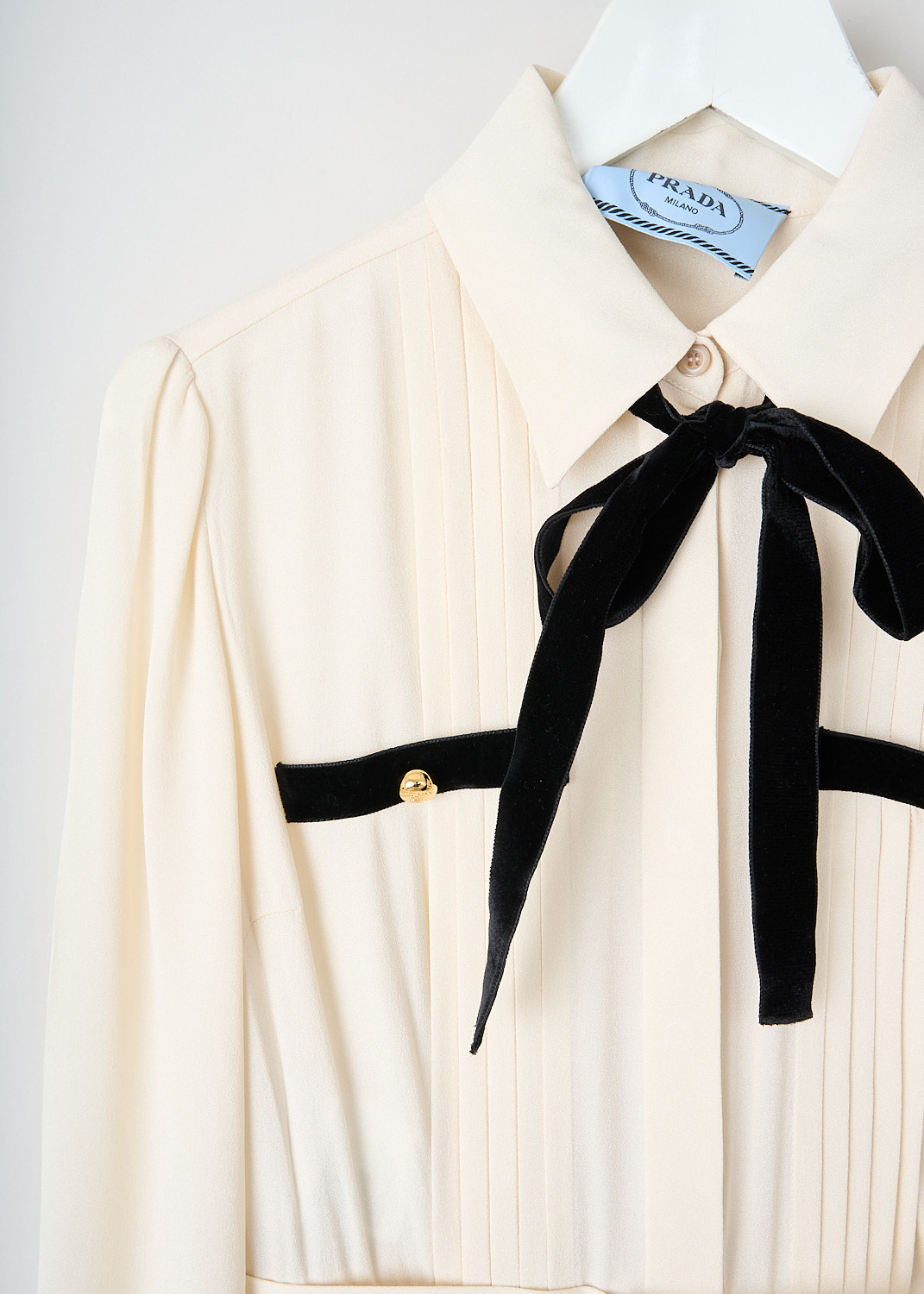 Close-up of black velvet bow, welt pocket trim, and gold-tone buttons on the Prada off-white satin maxi dress, available at Kiki's Stocksale in Maastricht.