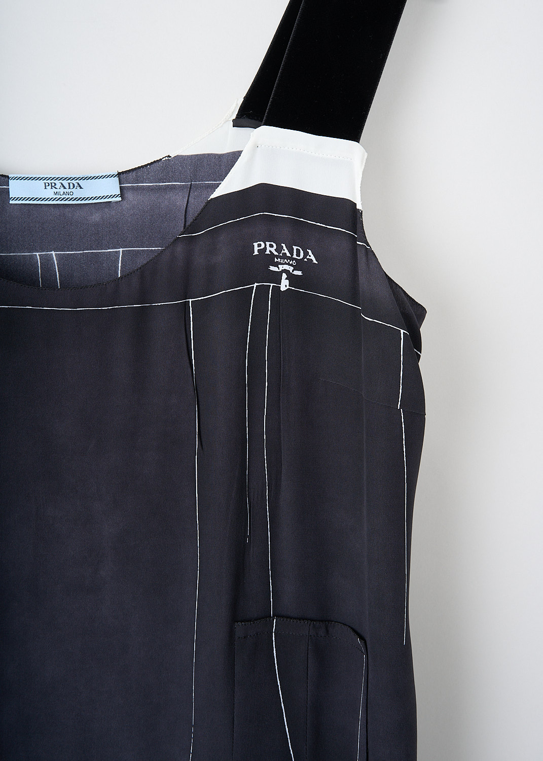 Prada, Black printed silk dress, 10R2_CREPEDECHINE_P3G58_F0002_NERO, Black, Detail, This black silk dress has a printed white pattern of thin lines. The dress has broad velvet shoulder straps and a round neckline. On the front, the brand's signature lettering logo van be found. A concealed side zip functions as the closure. The dress has a dropped-waist silhouette. 
