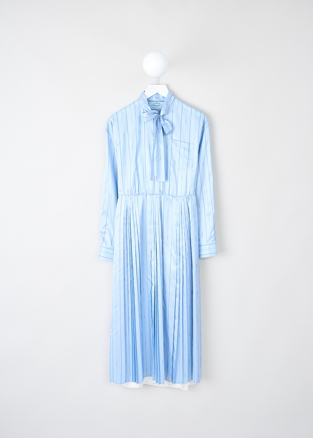 Prada, Light blue striped pleated dress, 11C5_PONGE_PRADA_P3H47_F0076_CELESTE, Blue, Front, This light blue striped pleated dress has a round neckline with a bow tie-detail. The long sleeves have buttoned cuffs. The bodice has a single breast pocket and a partial front button placket that stops at the waist. A concealed side zip functions as the closure. The midi skirt is pleated throughout. On the back of the neck, the brand's triangle logo can be found in the same fabric. The dress comes with a white slip dress. 
