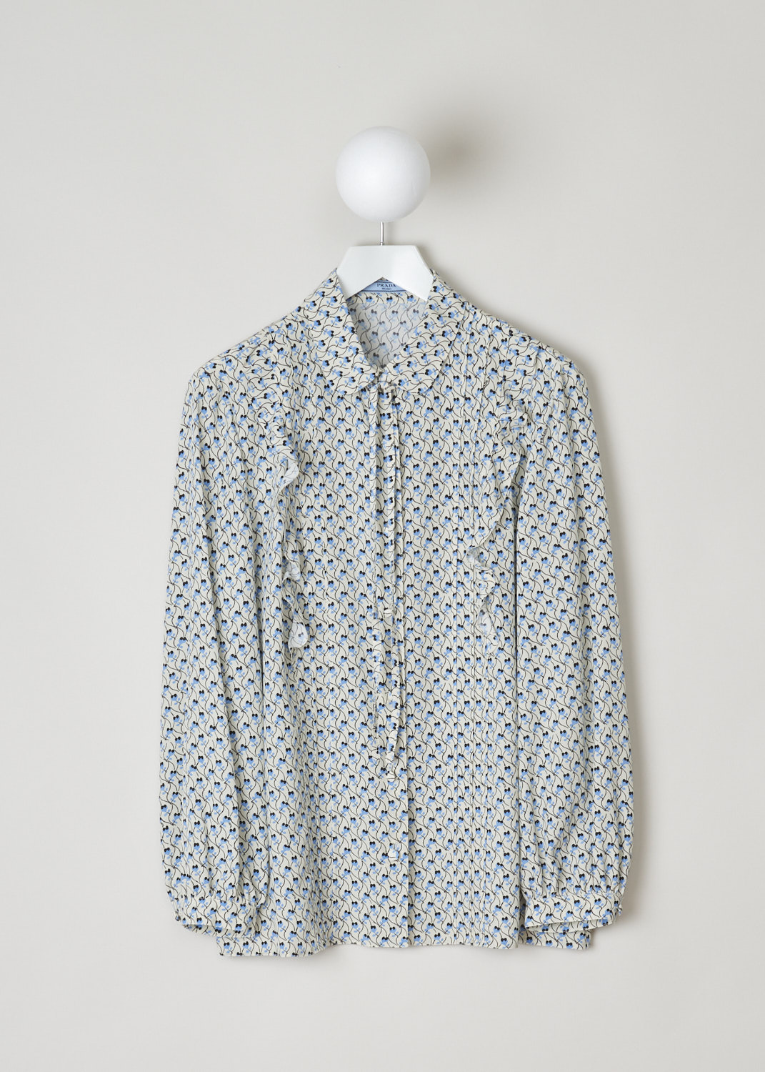Prada, Blouse with blue floral print, CDC_Ramage_P411E_F0304_avorio, Print, Blue, Front, This long sleeve blouse has a beige base color with a blue floral print. The blouse has a rounded collar with a pussy-bow and a front button closure. Subtle frills decorate the front. The long sleeves have buttoned cuffs. The blouse has a straight hemline.

