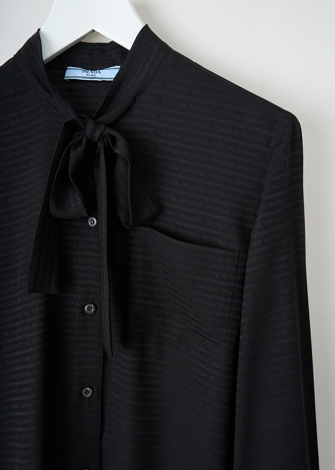 Close-up of the self-tie collar and single breast pocket of the black Prada blouse with logo print, available at Kiki's Stocksale in Maastricht.