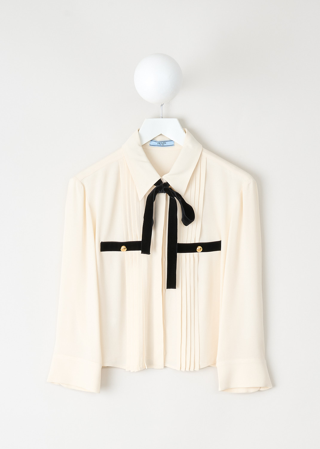 Off-white sablé blouse with black velvet bow collar, three-quarter sleeves, and front welt pockets with gold-tone buttons by Prada, available at designer boutique Kiki's Stocksale in Maastricht.