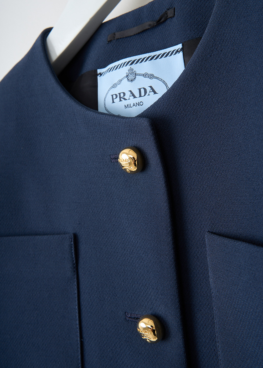 Close-up of gold-tone button front closure on cropped midnight blue tailored jacket with structured finish.