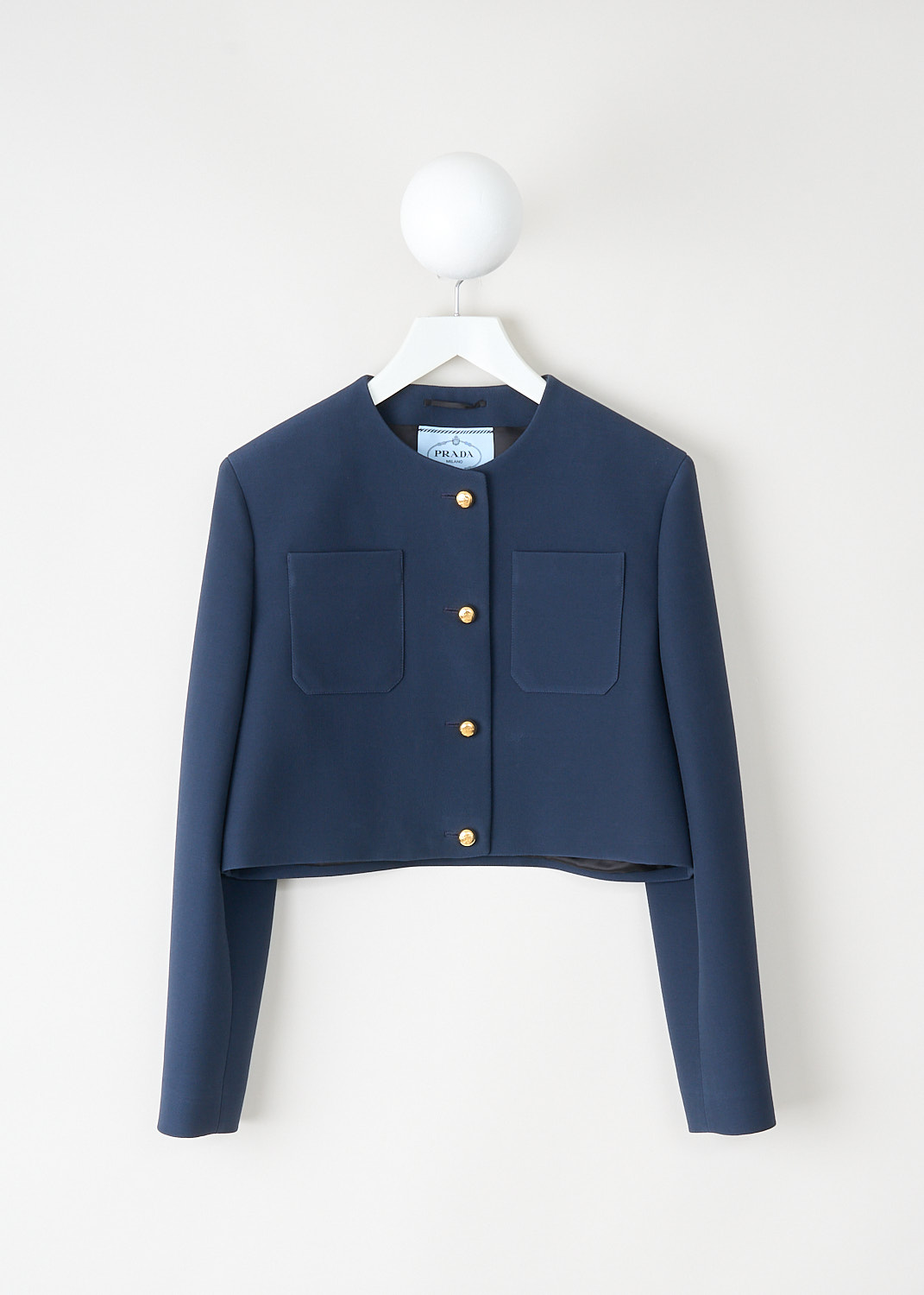 Cropped midnight blue wool-silk jacket with round neckline, shoulder pads, patch breast pockets and gold-tone button closure, available at Kiki’s Stocksale Maastricht designer outlet.