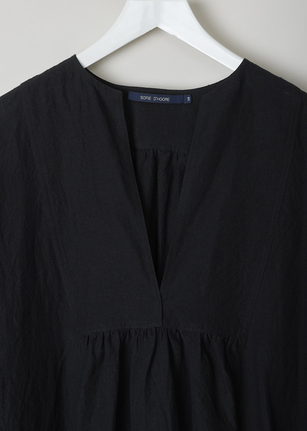 SOFIE Dâ€™HOORE, BLACK LINEN DELIZA DRESS, DELIZA_LIFE_BLACK, Black, Detail,This black linen dress has a round neckline that goes into a deep V cutout. Subtle ruching can be found beneath the V. This long sleeve midi dress has a straight hemline with an asymmetrical finish, meaning the back is a little longer than the front. The dress has concealed slanted pockets and slits can be found on either side. The dress has a wide silhouette. 

