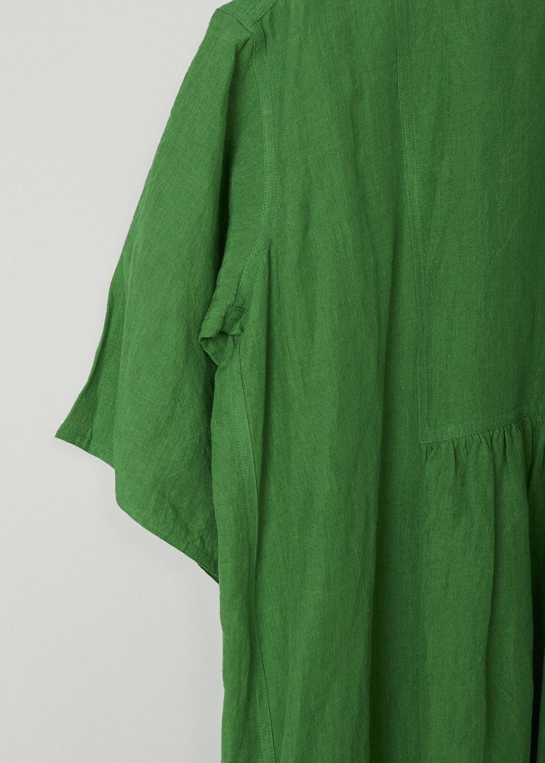 SOFIE Dâ€™HOORE, BRIGHT GREEN LINEN DARNELLE DRESS, DARNELLE_LIFE_GRASS, Green, Detail, This oversized green midi dress features a round neckline, dropped shoulders and short sleeves. The A-line dress has a square bib-like front with pleated details below. Concealed in the side seams, slanted pockets can be found. The dress has a straight hemline with slits on either side. 

