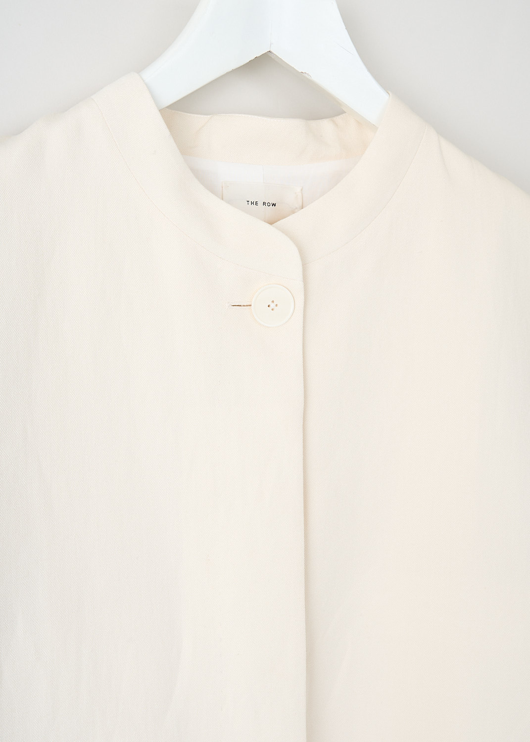 The Row, Aradia jacket in Ivory, ARADIA_JACKET_6011_W2166_IVORY, White, Detail, This Aradia jacket in Ivory has a mandarin collar with a single exposed button and a concealed front button closure. The long sleeves have buttoned cuffs. On the front, the jacket has welt pockets. In the back, the jacket has a centre vent. 
