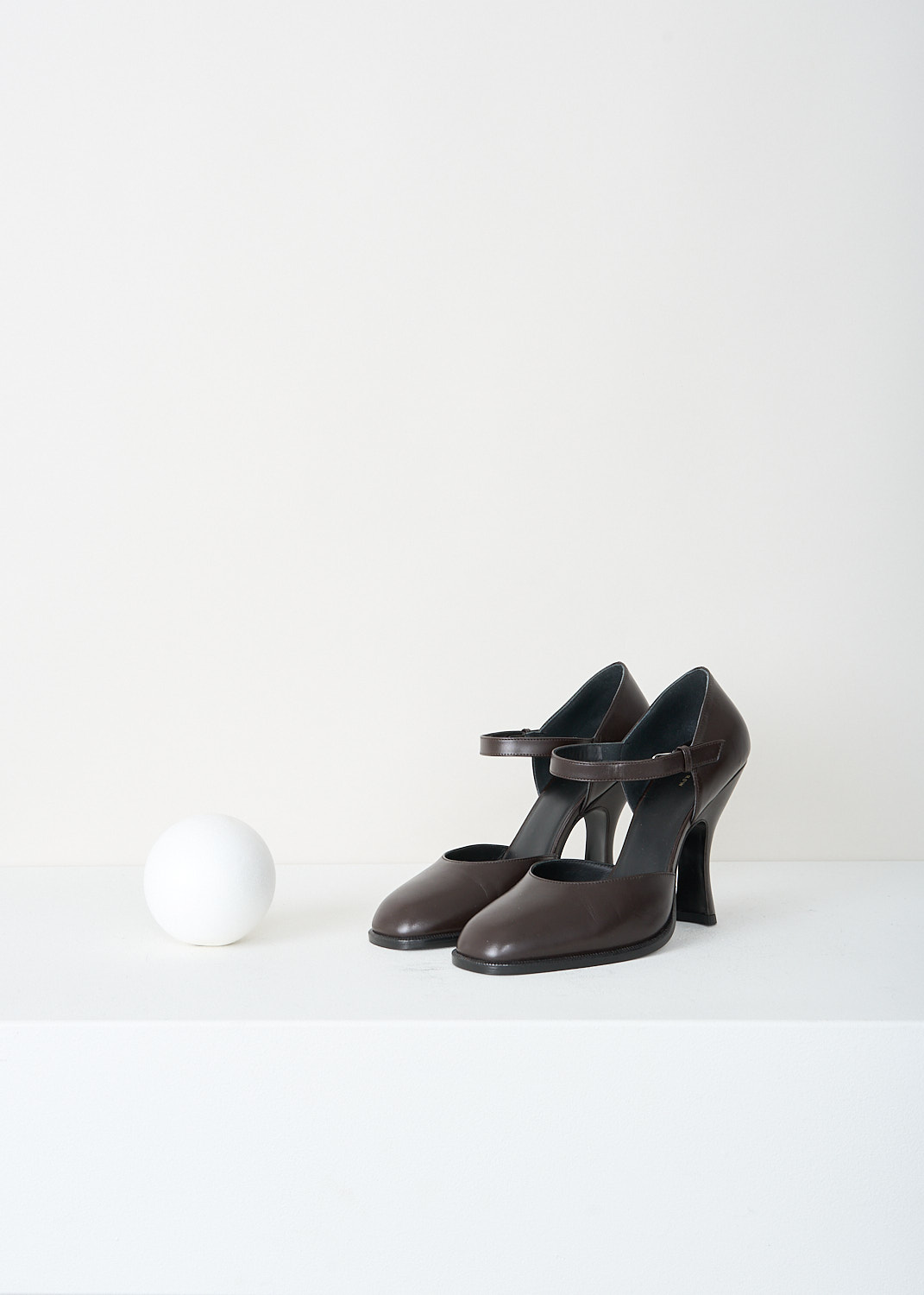 The Row, Mary-Jane pumps in Mocha, MARY_JANE_PUMP_F1195_L35_MOCHA, Brown, Front, These Mary-Jane pumps in the color Mocha have an ankle strap with an overlapping strap that hides the buckle closure. These pumps have an almond toe and a trapezoid heel.
