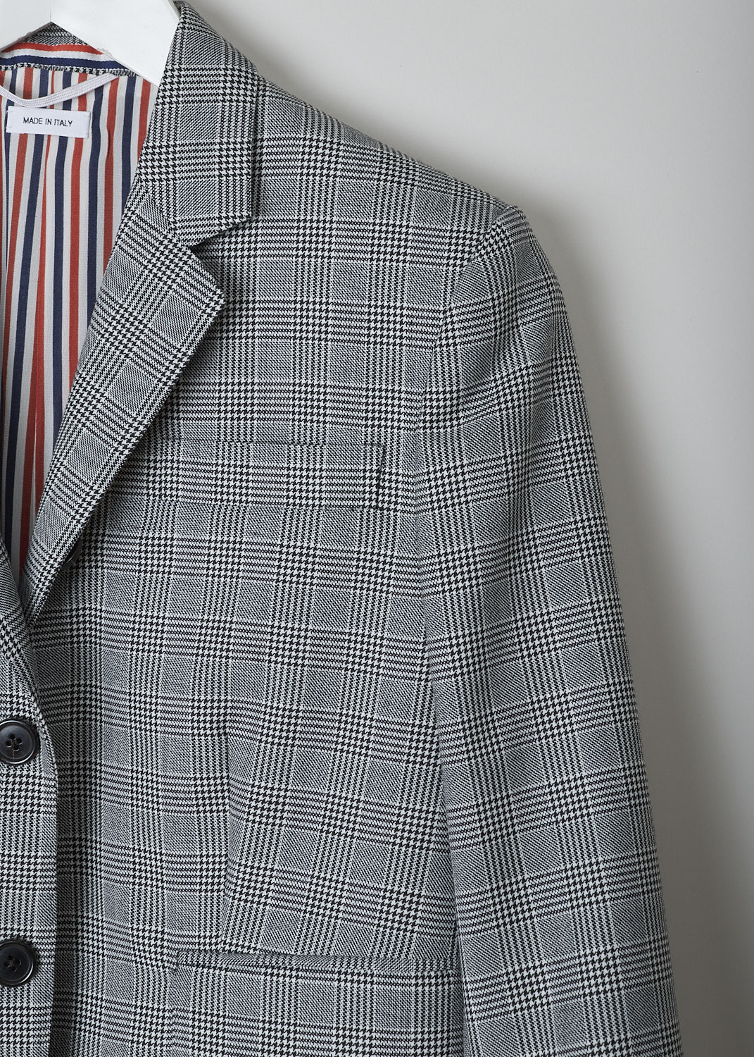 THOM BROWNE, BLACK AND WHITE CHECK SPORT JACKET, FBC010A_25057_980, Black, White, Detail, This single-breasted sport jacket has a black-and-white houndstooth check motif. The jacket has a notched lapel and a front button closure. In the front, the jacket has a single breast pocket and two flap welt pockets. On the inside, the jacket has a striped lining, three inner pockets and a name tag. The brand's signature striped grosgrain loop tab can be found in the back. The jacket has a double vent.
