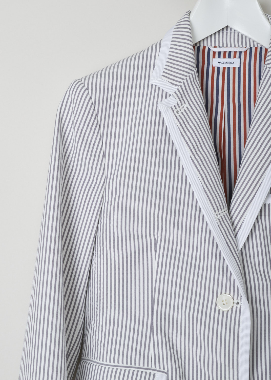 Thom Browne, white and grey striped blazer, FBC492B_00572_035, white grey, detail, Classic blazer reimagined with the seersucker cotton fabric, and the lovely striped motif. Featuring a collar that leads into the notched lapel, further decorating the front are two flap pockets and a single chest pocket. A notable feature here is that all the edges and hems are adorned with a white trim. On the back you will find two off-center splits. 