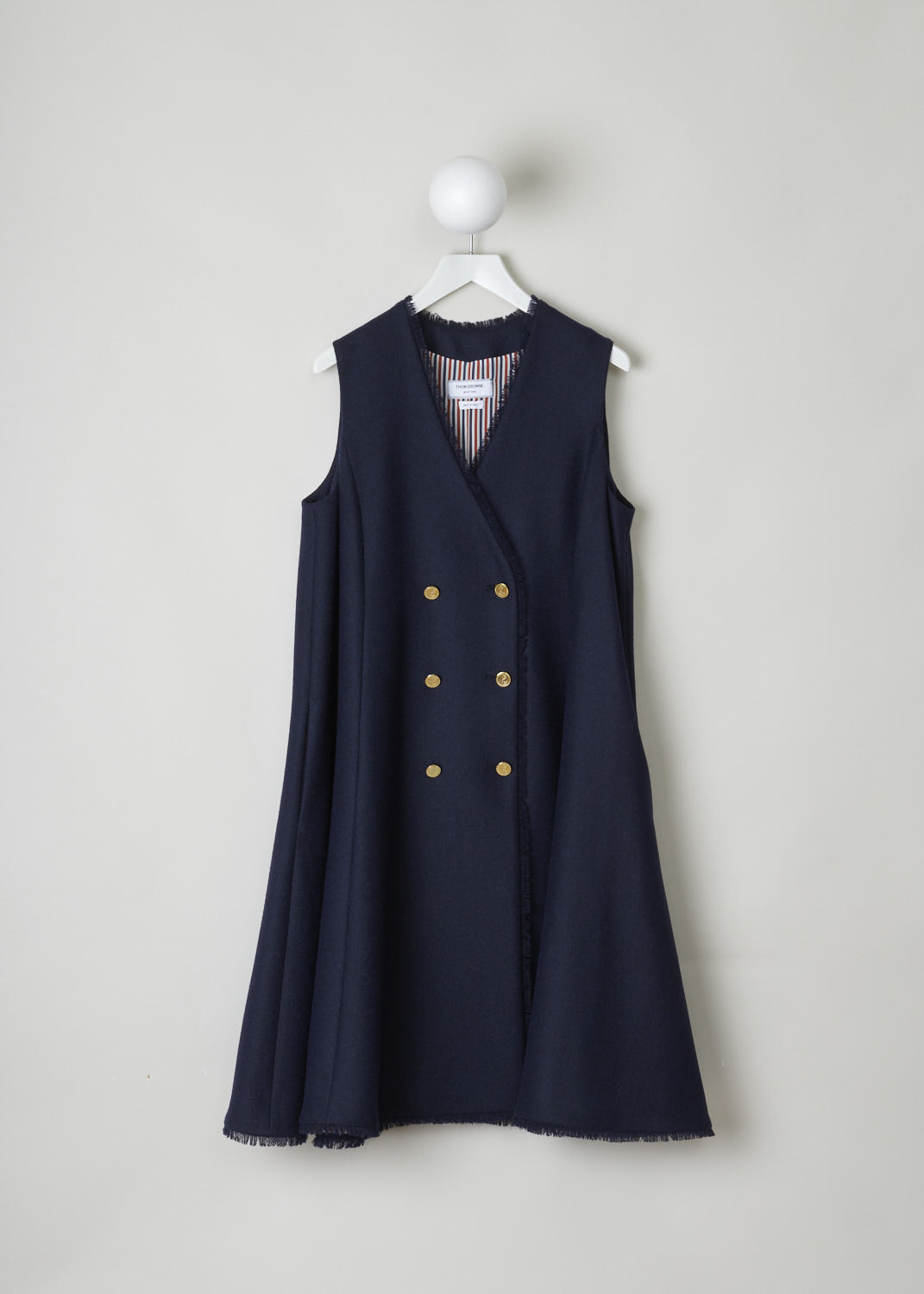 THOM BROWNE, NAVY BLUE A-LINE WAIST COAT DRESS, FDSB68T_03793_415, Blue, Front, Structured, navy blue sleeveless waistcoat dress. The model has an A-line silhouette. This garment has a V-neck and a double breasted front, with golden-tone buttons. The hem has frayed edges. On either side, concealed pockets can be found along the seams. In the back, a rear slit can be found, decorated with a single golden-tone button. In the neck, the signature tri-colored tab can be found.

