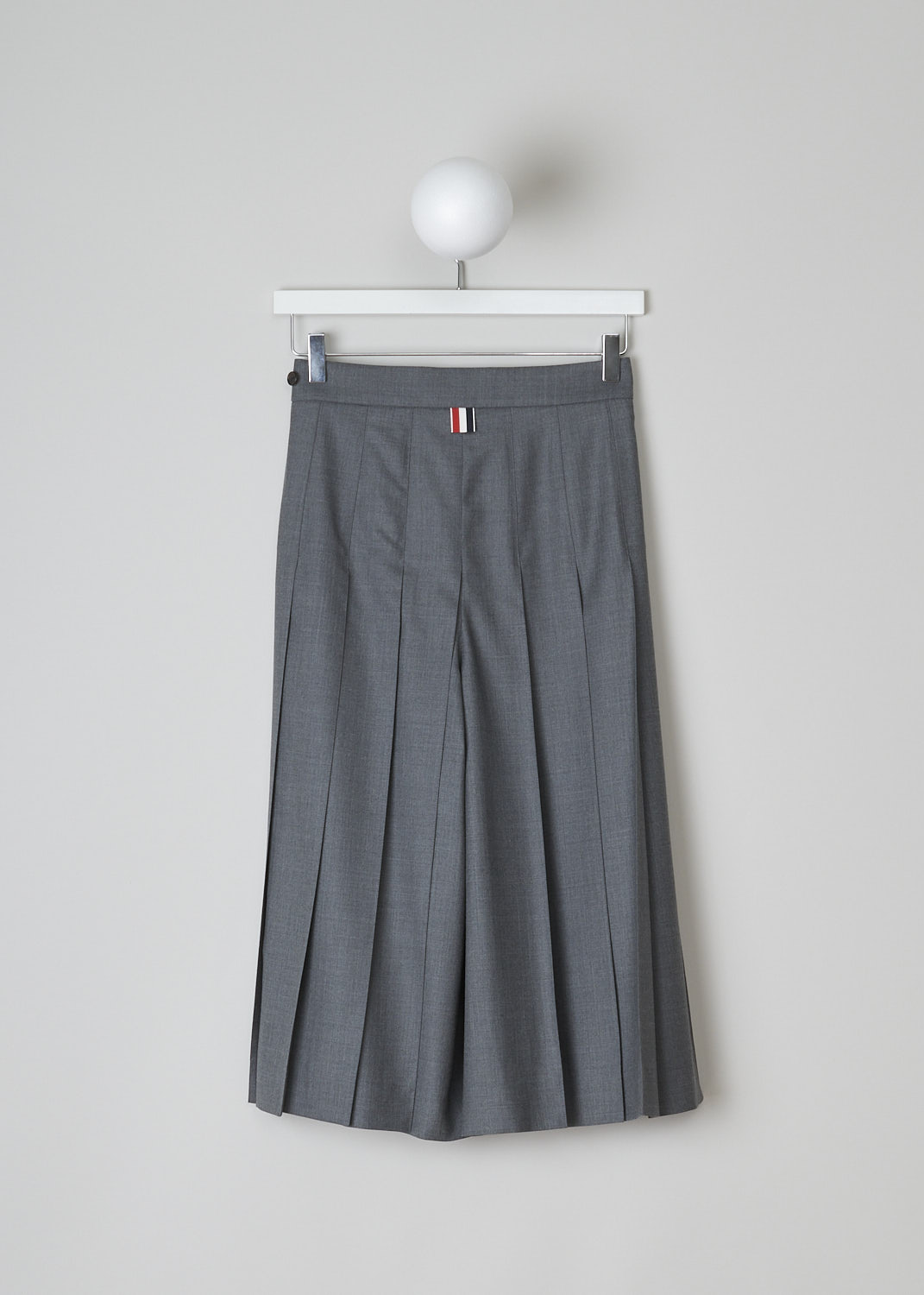 THOM BROWNE, PLEATED CULOTTES IN MID GREY, FTC379A_00626_035, Grey, Back, These mid grey pleated culottes have a concealed zip closure to one side with a button tab on the waistband. These culottes hit below the knee. In the back, the brand's signature tricolored pull-tab can be found.
