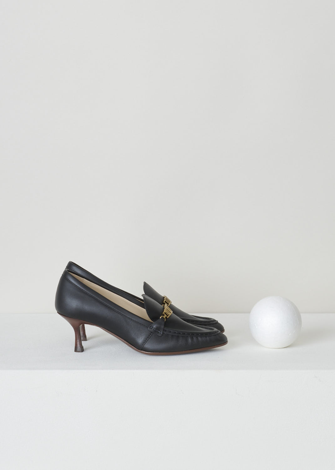 TODS, BLACK LEATHER LOAFERS WITH A TRAPEZOID HEEL, XXW09D0EC80_MID_B999_NERO, Black, Side, Black leather loafers with a wooden spool heel. This model has a pointed toe and a gold-tone buckle decorating the front. Around the trim, the leather is subtly pleated.
