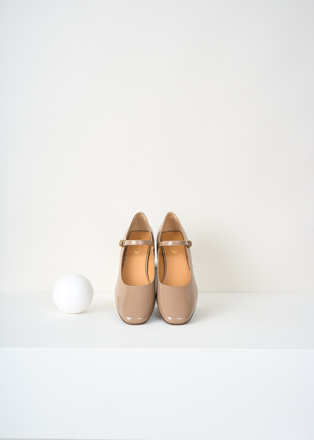Top view of Tod’s beige patent leather pumps highlighting the classic Mary Jane strap and branded gold-tone buckle detail – luxury fashion footwear at Kiki’s Stocksale designer boutique Maastricht.
