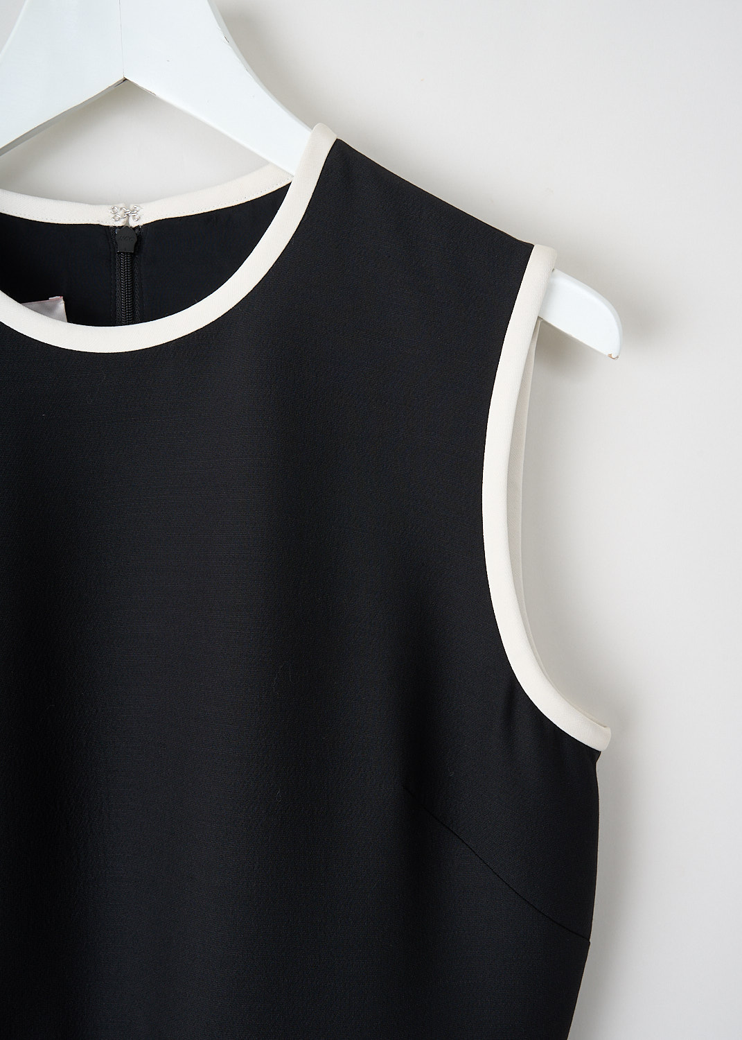 Close-up of round neckline and white contrast piping on black sleeveless mini dress with clean luxury finish.
