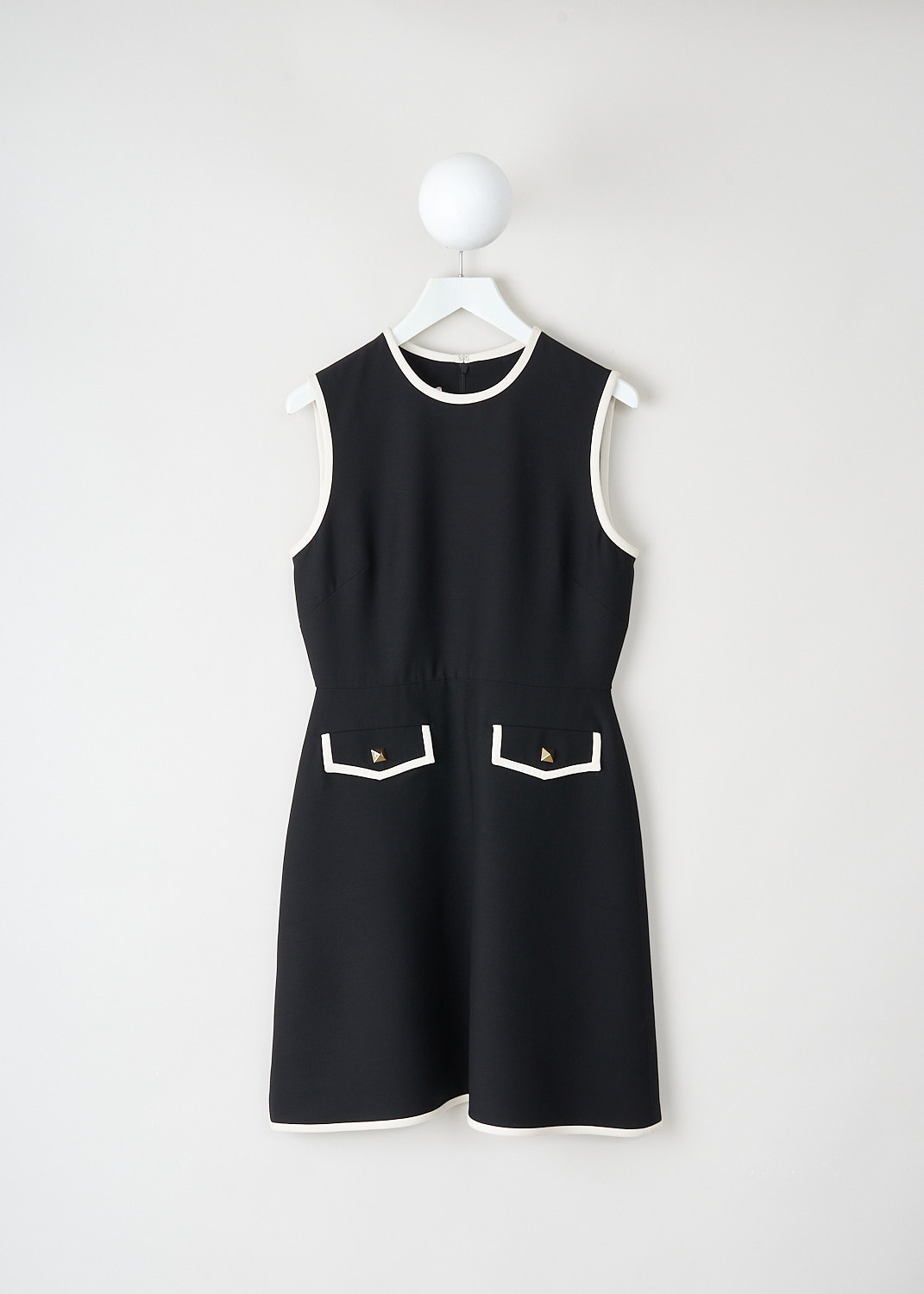 Black slim fit mini dress with round neckline, sleeveless design, white contrast piping and flap welt pockets with gold-tone buttons, available at Kiki’s Stocksale Maastricht designer outlet.