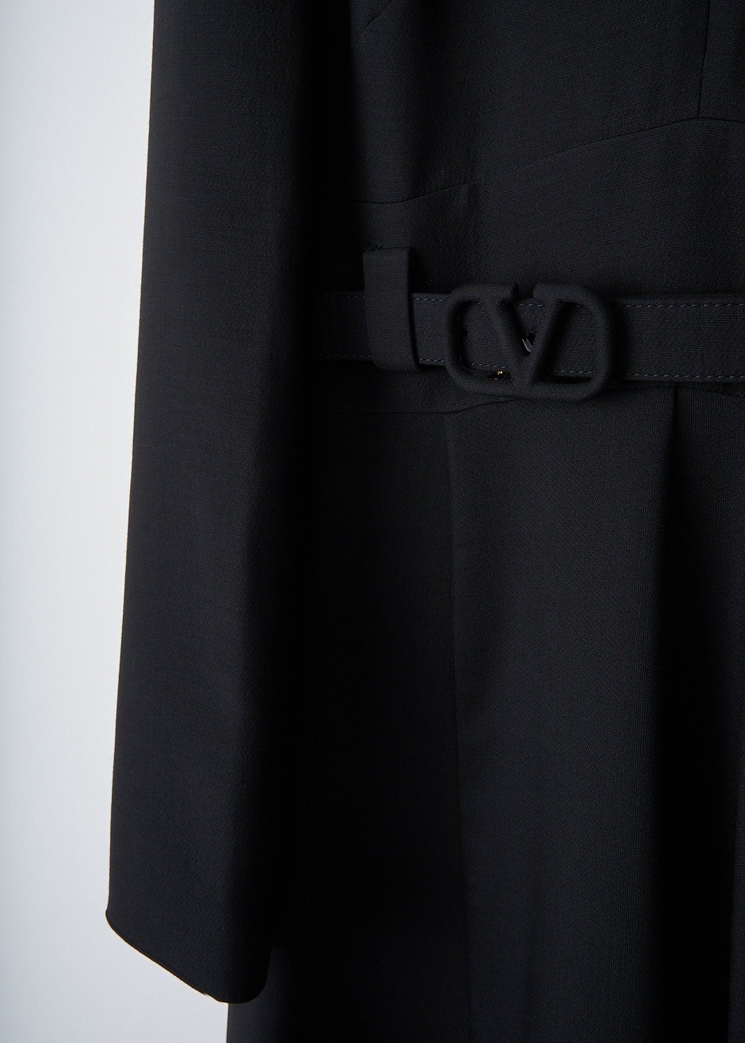 Close-up detail of Valentino black wool-blend dress showing broderie anglaise hem, front zipper and V-buckle belt